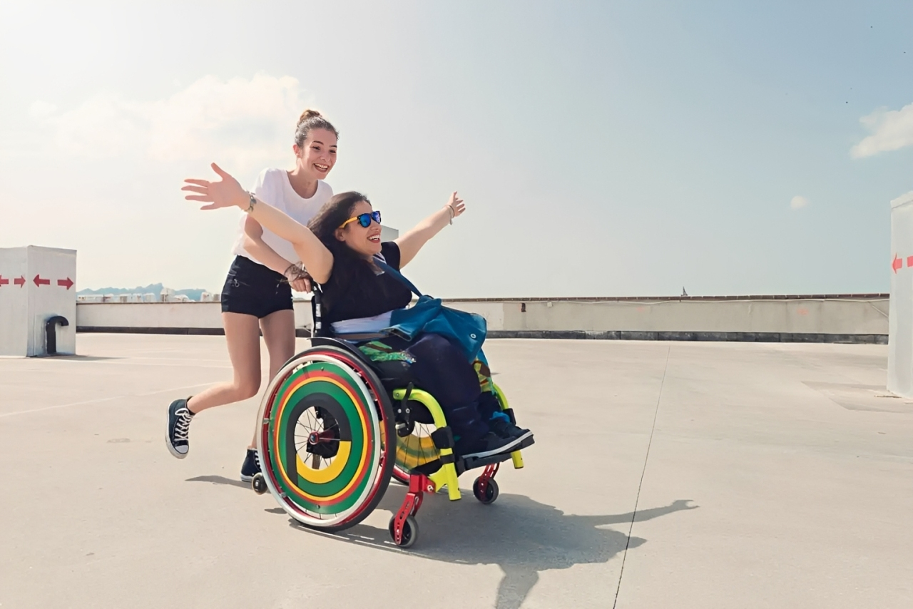 Carer pushing a girl in a colourful wheelchair
